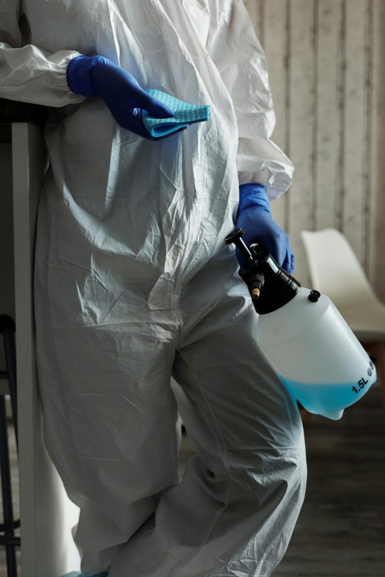 Person in PPE suit and gloves with disinfectant and cloth cleaning indoors.